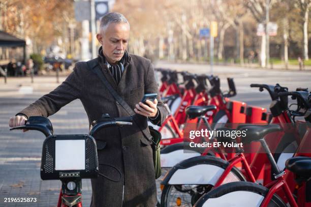 mature businessman renting a bicycle in a bike sharing station using a smartphone app - sharing economy stock-fotos und bilder