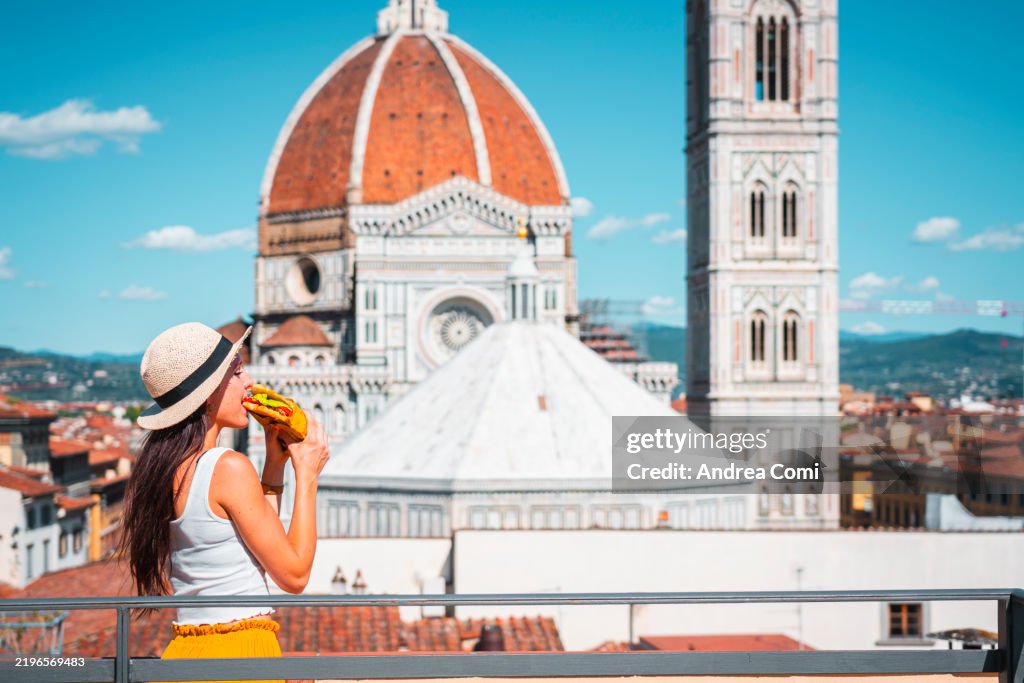 Young woman enjoying a sandwich on rooftop with Florence Cathedral in background, Florence, Italy