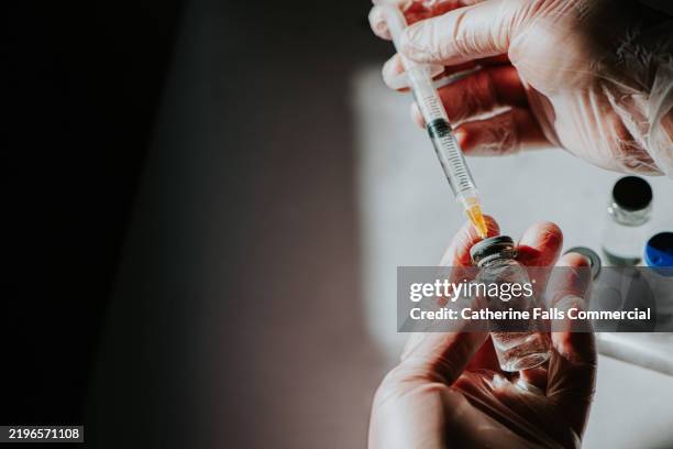 a healthcare professional uses a syringe to draw liquid medicine from a vial. - medische artikelen stockfoto's en -beelden