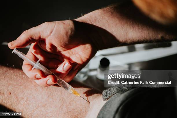 a person administers an injection in their own arm using a small syringe - drogados imagens e fotografias de stock