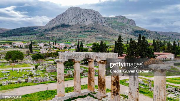 aerial view of ancient corinth with the temple of apollo and surrounding ruins, historical site in greece with mountain backdrop and lush greenery, cultural heritage and tourism concept - templo de apolo corinto imagens e fotografias de stock