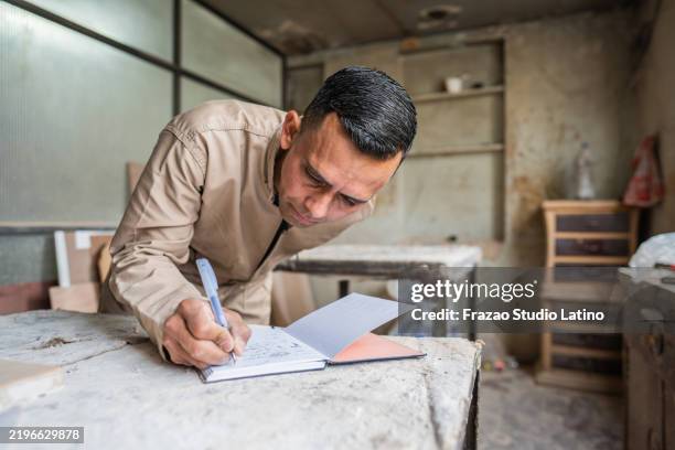 amputee carpenter writing on note pad on a woodshop - jumpsuit stock pictures, royalty-free photos & images