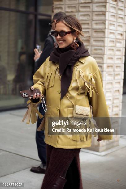 Guest wears dark brown knitted long skirt, brown scarf, mustard green leather jacket with tassels outside the Herskind fashion show during the...