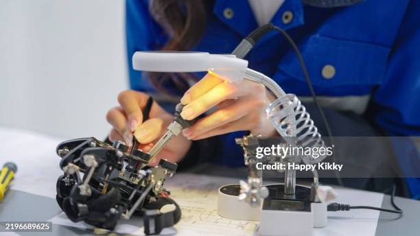 close up woman engineer developer wearing safety protective goggles with blue work jacket is soldering intricate robotic components on a circuit board or an electronic device workshop in a laboratory room - mechatronics stockfoto's en -beelden