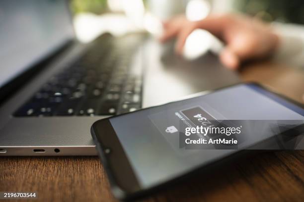 mann mit smartphone und laptop versucht, sich mit zwei-faktor-authentifizierung anzumelden. datensicherheitskonzept. - digitale authentifizierung stock-fotos und bilder