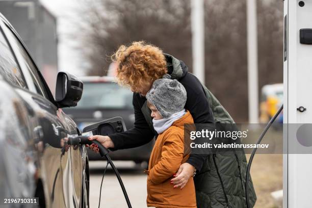 woman and child charging an electric vehicle with charging handle in their hands. - electric car stock pictures, royalty-free photos & images