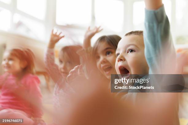 a group of small children with their hands raised in a kindergarten - nursery school building stock pictures, royalty-free photos & images