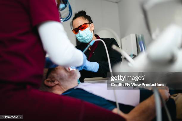 zahnärztin und männlicher assistent führen eine untersuchung des älteren patienten durch - dentalhygieniker stock-fotos und bilder