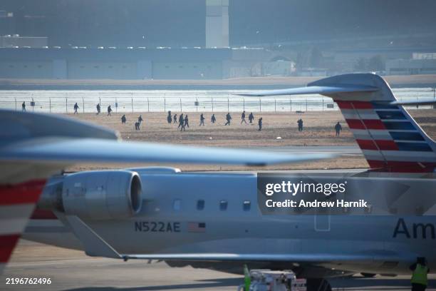 Investigators walk the grounds of the Reagan National Airport as they work after the crash last night of the American Airlines plane on the Potomac...