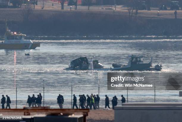 Investigators walk the grounds of the Reagan National Airport as they work near the crash last night of the American Airlines plane on the Potomac...