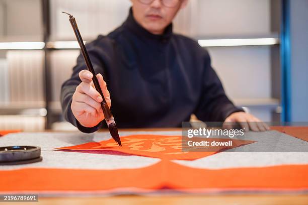 chinese man writes spring festival couplets with a chinese brush - chinesisches schriftzeichen stock-fotos und bilder