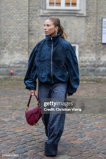 Guest wears blue jacket, Dior saddle bag, wrapped wide leg denim jeans outside TG Botanical during the Copenhagen Fashion Week Autumn/Winter 2025 on...