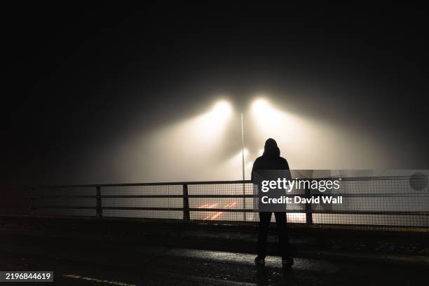 a sinister hooded figure, standing above a motorway. on a mysterious foggy night. silhouetted by street lights - missing persons stock pictures, royalty-free photos & images