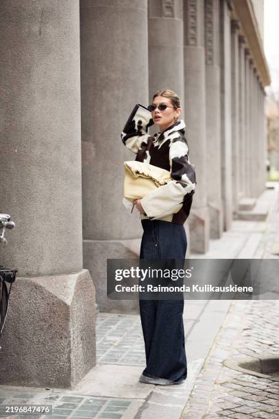 Sophia Geiss wears cow print cropped jacket with a zipper, pale yellow bag, blue wide jeans during the Copenhagen Fashion Week Autumn/Winter 2025 on...