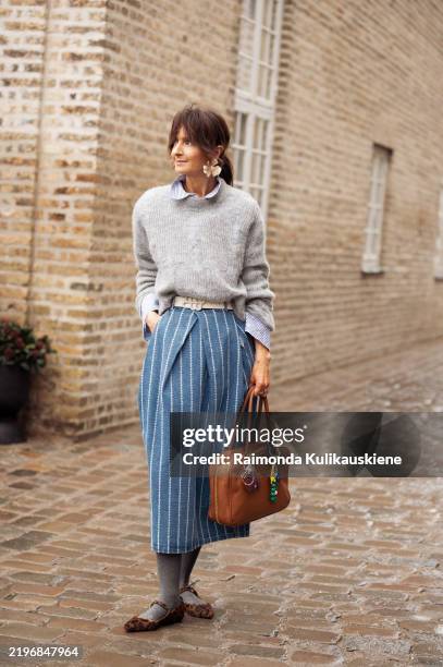 Guest wears grey sweater, blue denim skirt, brown bag with accessories and animal print shoes outside the Munthe fashion show during the Copenhagen...