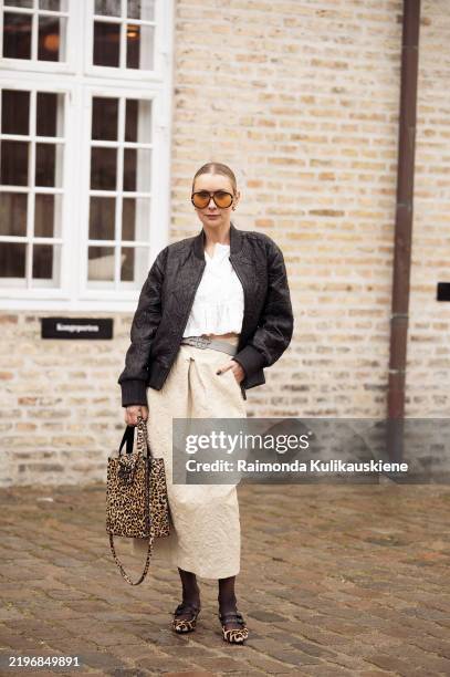 Justyna Czerniak wears beige long skirt, white crop top, black leather jacket, animal print bag, orange sunglasses and animal print shoes outside the...