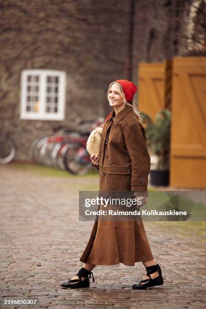Hollie Mercedes Peters wears brown skirt, brown suede jacket, beige bag, red head scarf and black shoes outside the Munthe fashion show during the...