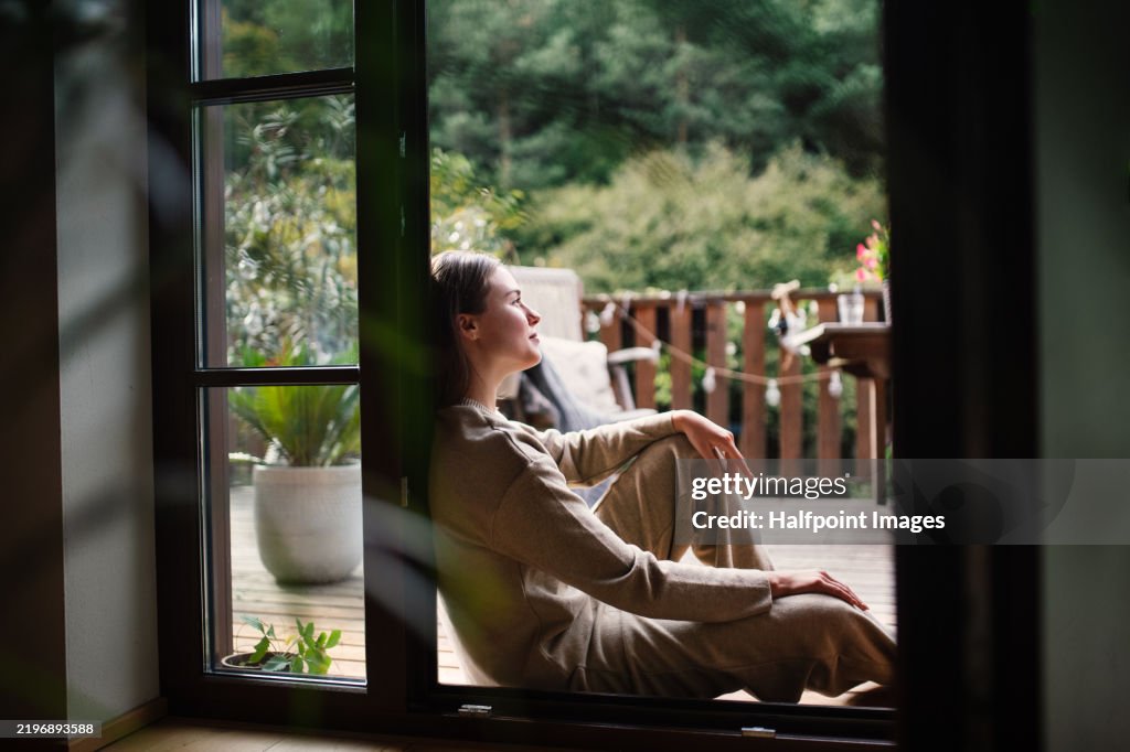 Woman resting in doorway of balcony doors, resting. Single woman enjoying free weekend. Concept of selfcare.
