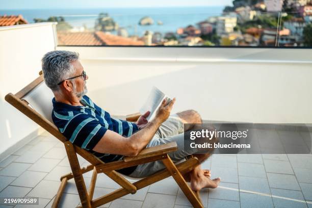 man reading a book on the balcony - zuid europese etniciteit stockfoto's en -beelden
