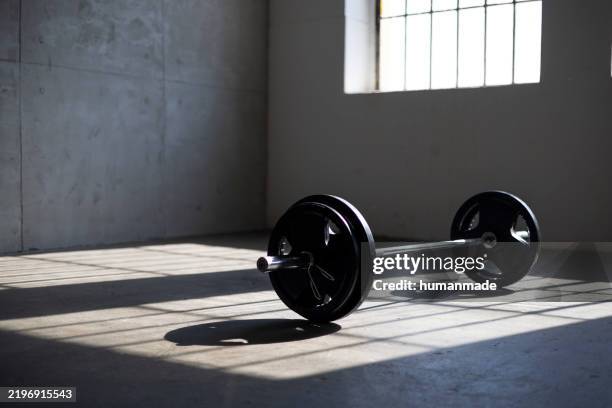 barbell resting on floor in empty gym with sunlight streaming through window - halterofilismo imagens e fotografias de stock
