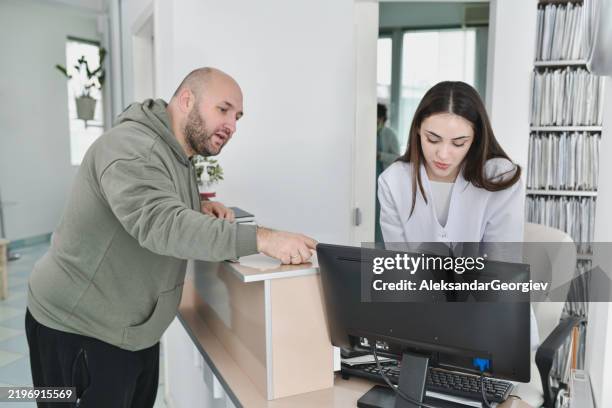 male patient and nurse looking at free appointment slots on computer at reception desk - tandartsassistent stockfoto's en -beelden