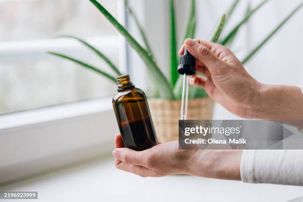 woman holding glass dropper bottle with natural essential oil - massageöl stock-fotos und bilder