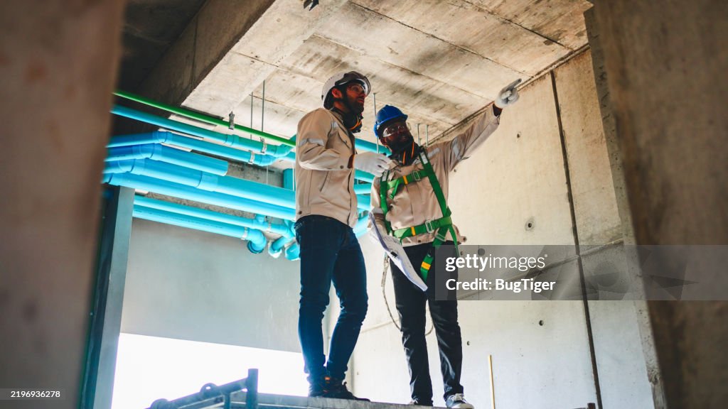 Male builder measuring plastic pipes with new home construction.