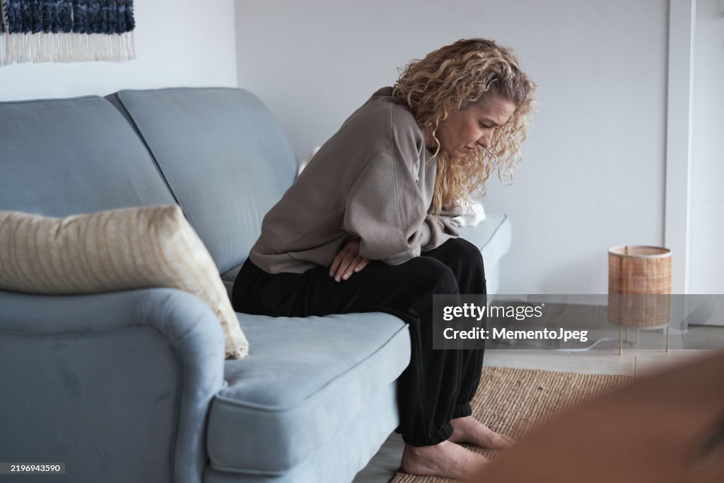 Menopause. Sad depressed middle-aged woman sitting on sofa at home, feeling anxious during perimenopause. Upset lonely mature female coping with divo