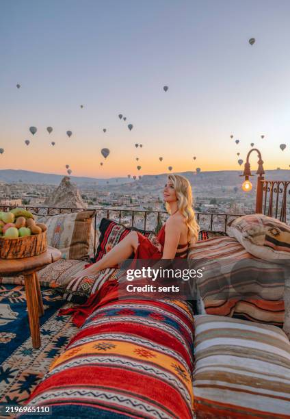 woman enjoying hot air balloons at sunrise from a traditional terrace in cappadocia, turkey - cappadocia stock pictures, royalty-free photos & images