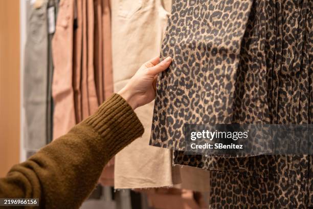 woman choosing leopard print pants in clothing store - leopard print stock pictures, royalty-free photos & images