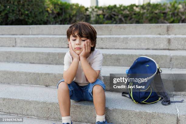 sad child sitting on stairs with backpack, feeling lonely and bored - endurance stock pictures, royalty-free photos & images