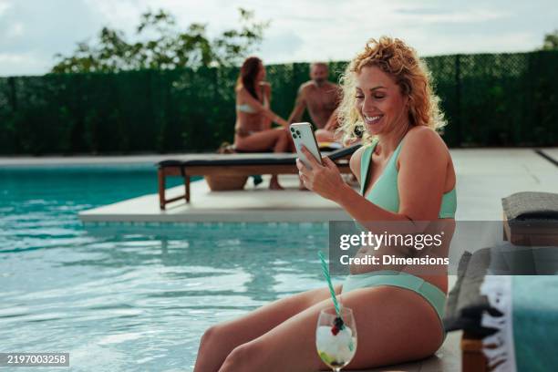 mujer sonriente mirando su teléfono inteligente junto a la piscina - al lado de fotografías e imágenes de stock