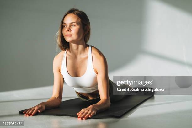 young slim woman in sportswear doing stretching on mat in modern studio - postura foto e immagini stock