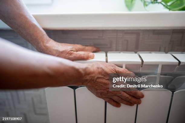 woman hands rest on heating radiator checking warmth. struggling in winter, energy crisis, cold home - gas appliance stock pictures, royalty-free photos & images