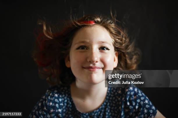 niña de 7 años sonríe con el pelo azotado por el viento sobre un fondo oscuro. - música cinematográfica fotografías e imágenes de stock