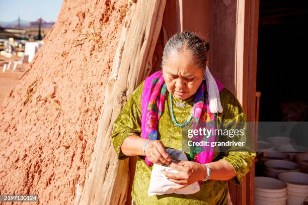 elderly traditional navajo native american woman in traditional dress at doorway of her hogan dwelling smiling at camera and holding medicinal herbs used to heal ailments using traditional navajo techniques - traditional native american medicine stock pictures, royalty-free photos & images