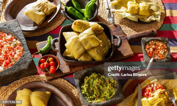 traditional chilean tamales - humitas, a dish made with corn masa wrapped in corn husks with fresh tomatoes sauces salsa and avocado guacomole in stone mortar. - chili pepper stockfoto's en -beelden
