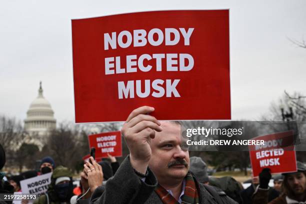 People hold up signs as they protest against US President Donald Trump and Elon Musk's "Department of Government Efficiency" outside of the US...