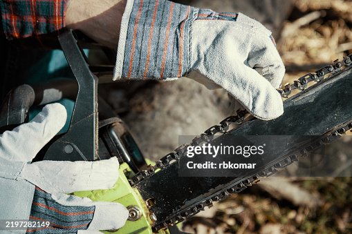 Worker performs precise chainsaw maintenance outdoors. Gloved hands carefully adjust tension on industrial cutting chain Worker performs precise chainsaw maintenance outdoors. Gloved hands carefully adjust tension on industrial cutting chain
