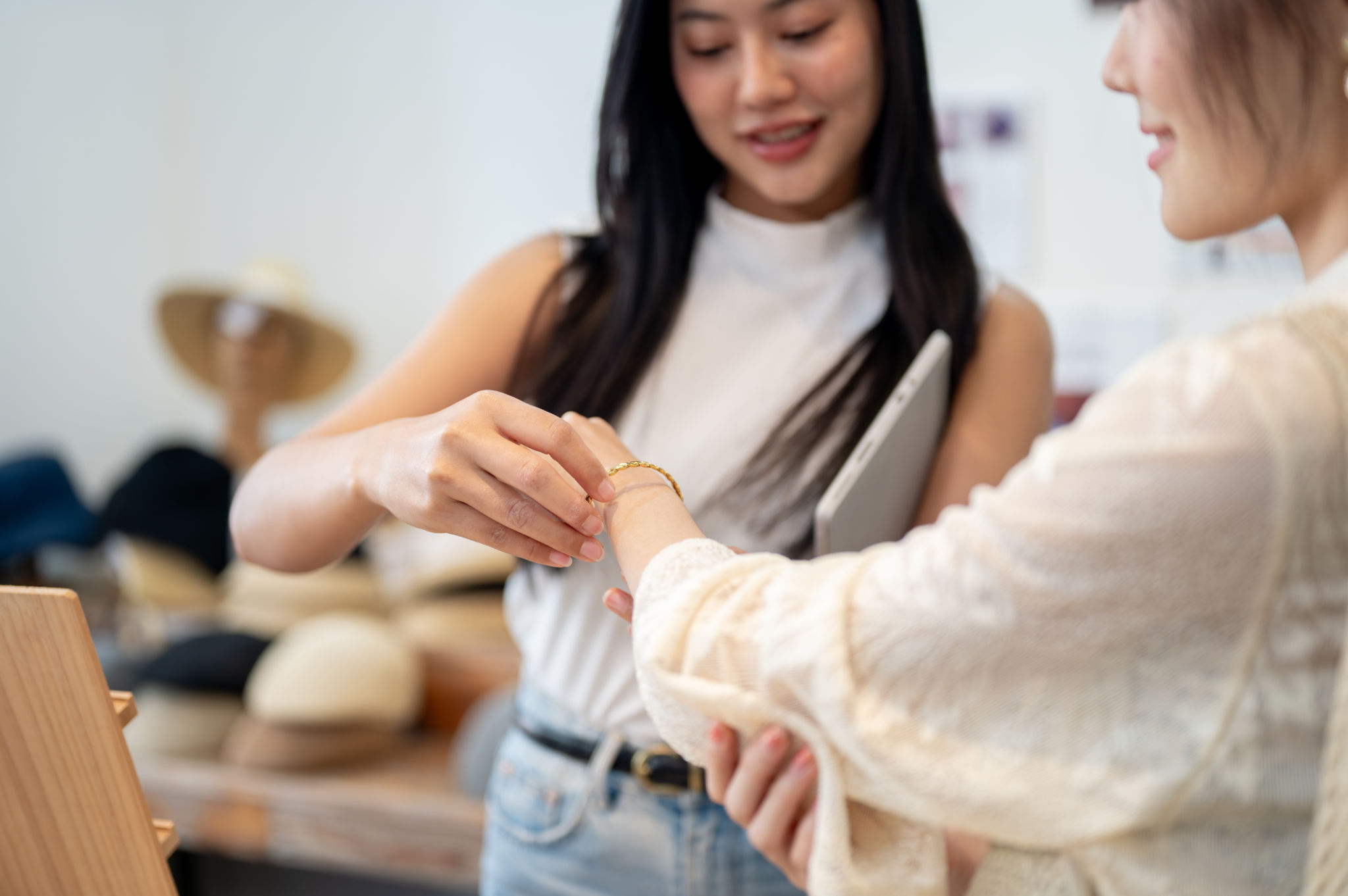 A close-up of a friendly Asian female shop employee is helping a customer try on a bracelet. A close-up of a friendly Asian female shop employee is helping a customer try on a bracelet.