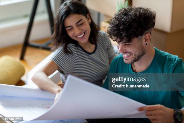 young couple examining blueprint of new home - model home stock pictures, royalty-free photos & images