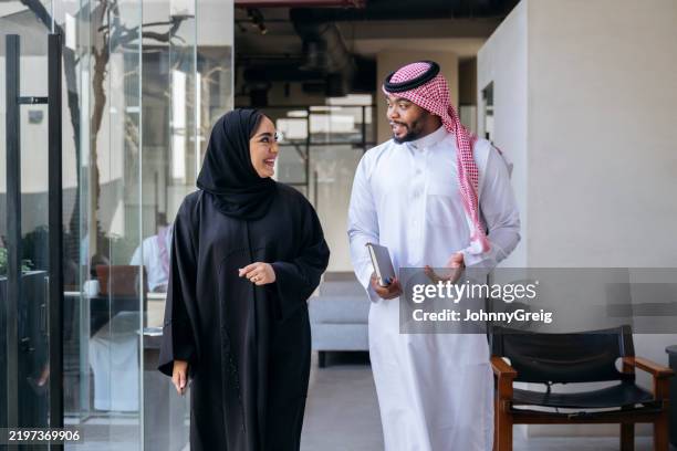 homme d’affaires marchant et parlant avec une collègue dans un bureau moderne, vêtu de vêtements traditionnels du moyen-orient - culture saoudienne photos et images de collection