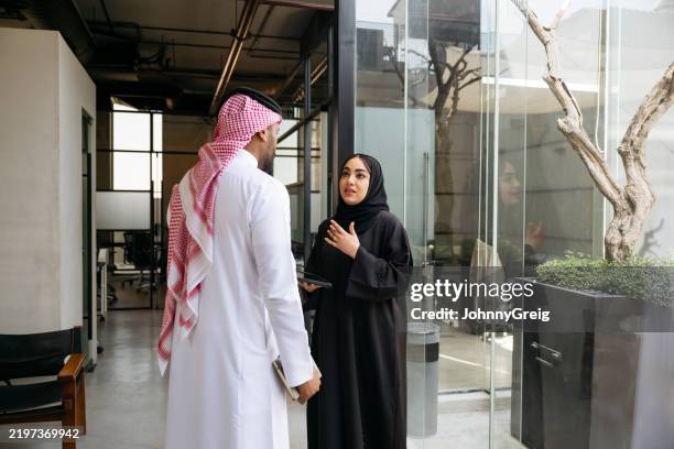 une femme cadre du moyen-orient portant un hijab et une abaya explique à un collègue masculin dans un bureau moderne - culture saoudienne photos et images de collection