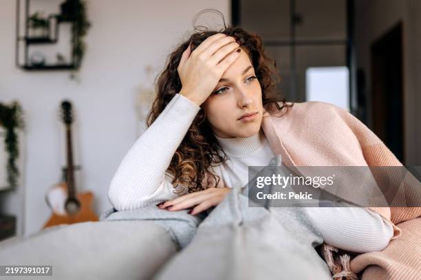 müde junge frau, die in eine decke gehüllt auf einem sofa liegt - winterdepression stock-fotos und bilder