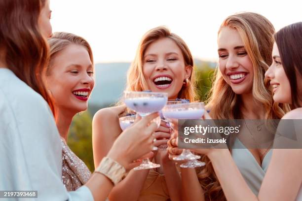 female friends wearing elegant dresses drinking lavender drinks outdoors at sunset - formal party stock pictures, royalty-free photos & images