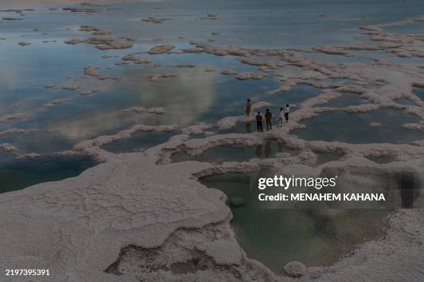 People walk on patterns formed by crystalized minerals on the surface of evaporation ponds in the Dead Sea, near the Israeli resort of Ein Bokek on...