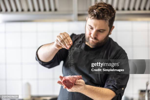 chef seasoning beef steak with salt and pepper in commercial kitchen. preparing beef wellington. - boucher photos et images de collection