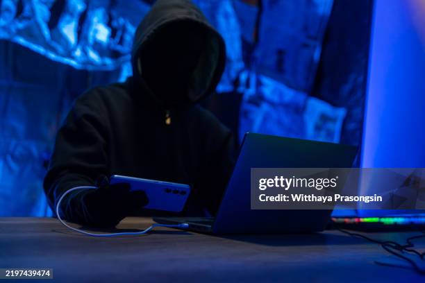 hacker using laptop and smartphone in a dimly lit room - corporate theft stock pictures, royalty-free photos & images