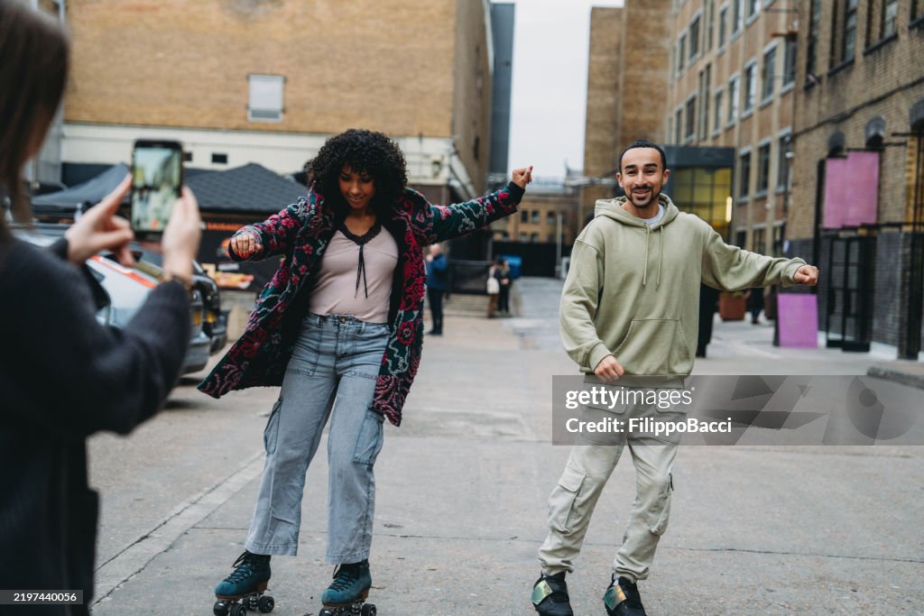 Young couple roller skating and dancing while being filmed by a friend
