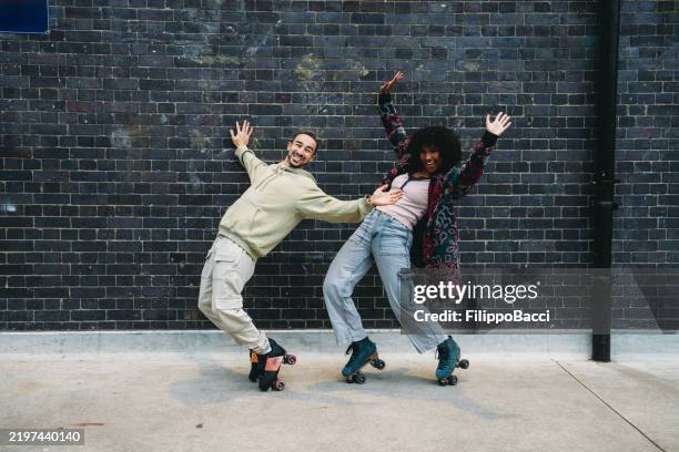 young couple having fun roller skating against a brick wall - roller skates stock pictures, royalty-free photos & images